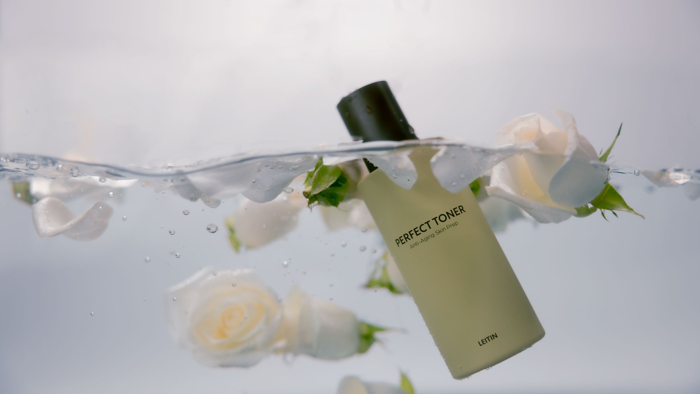 Image of LEITIN Skincare's Perfect Toner submerged in water and white roses.